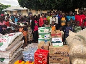 Community members standing behind stacked relief items — bags of grain, cartons and mattresses — at the Rimau IDP camp.