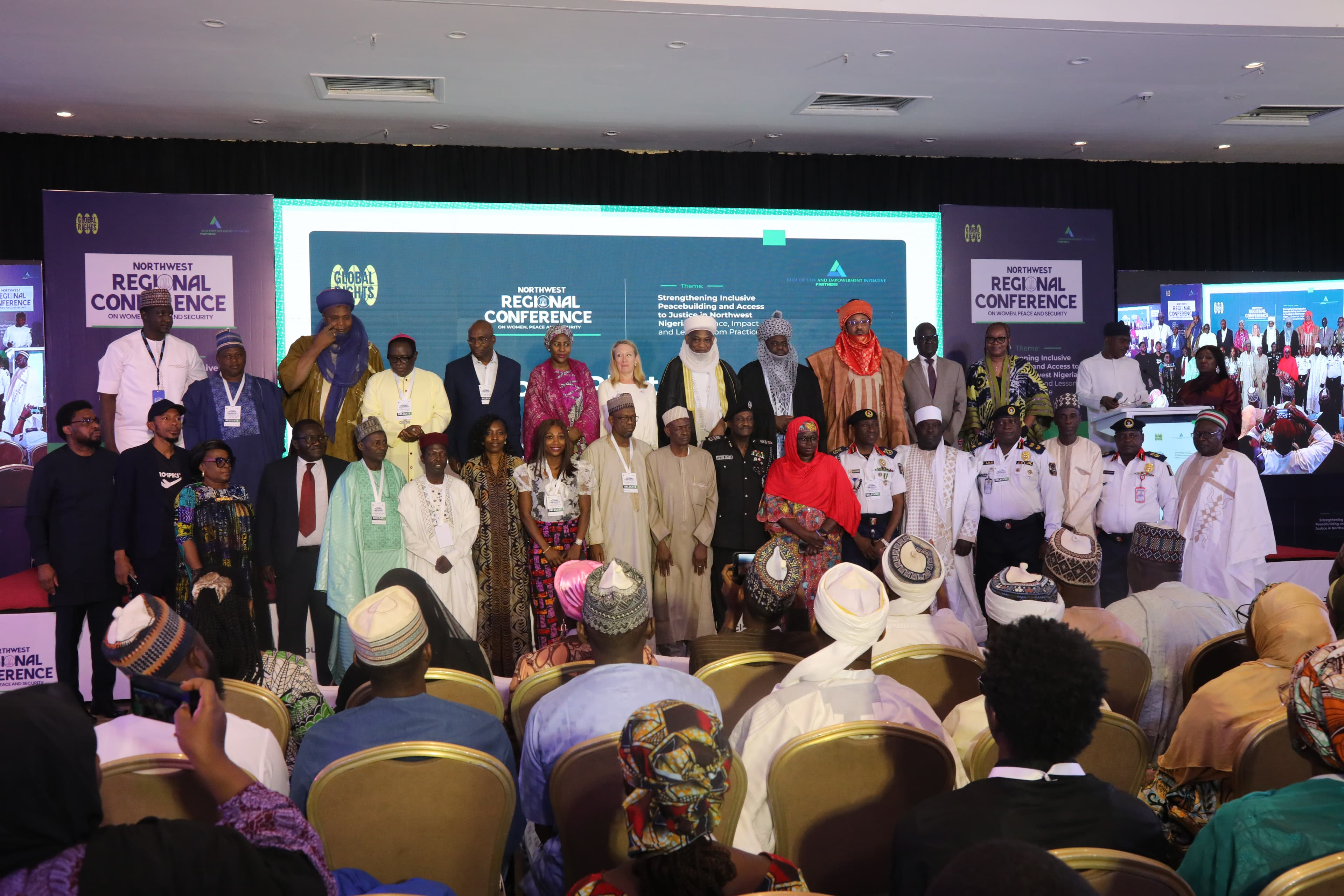 Delegates, traditional rulers, security officers and civil society representatives standing together on stage at the Northwest Regional Conference on Women, Peace and Security, before a screen reading “Strengthening Inclusive Peacebuilding and Access to Justice in Northwest Nigeria: Impact and Lessons from Practice”.