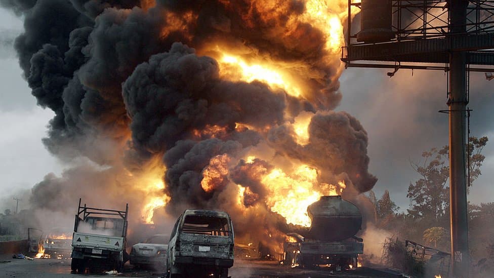A petrol tanker ablaze on a road, black smoke rising above burnt-out vehicles.